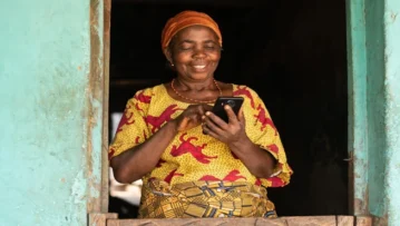 An older African femme-presenting person glances at a mobile device in their hand lovingly.