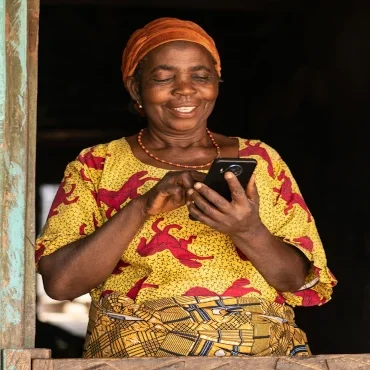 An older African femme-presenting person glances at a mobile device in their hand lovingly.