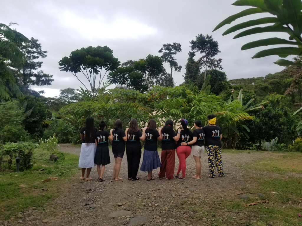 Nine members of the Whose Knowledge? team stand next to each other in the rainforest during a retreat in Costa Rica.