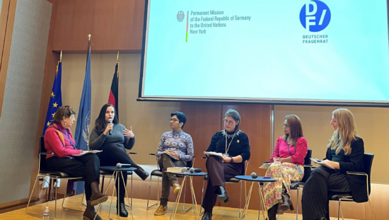 Five femme-presenting speakers sit next to each other on a stage. On the background, there are flags and a screen sharing the logos of the German Mission to the United Nations and the National Council of German Women's Organisations